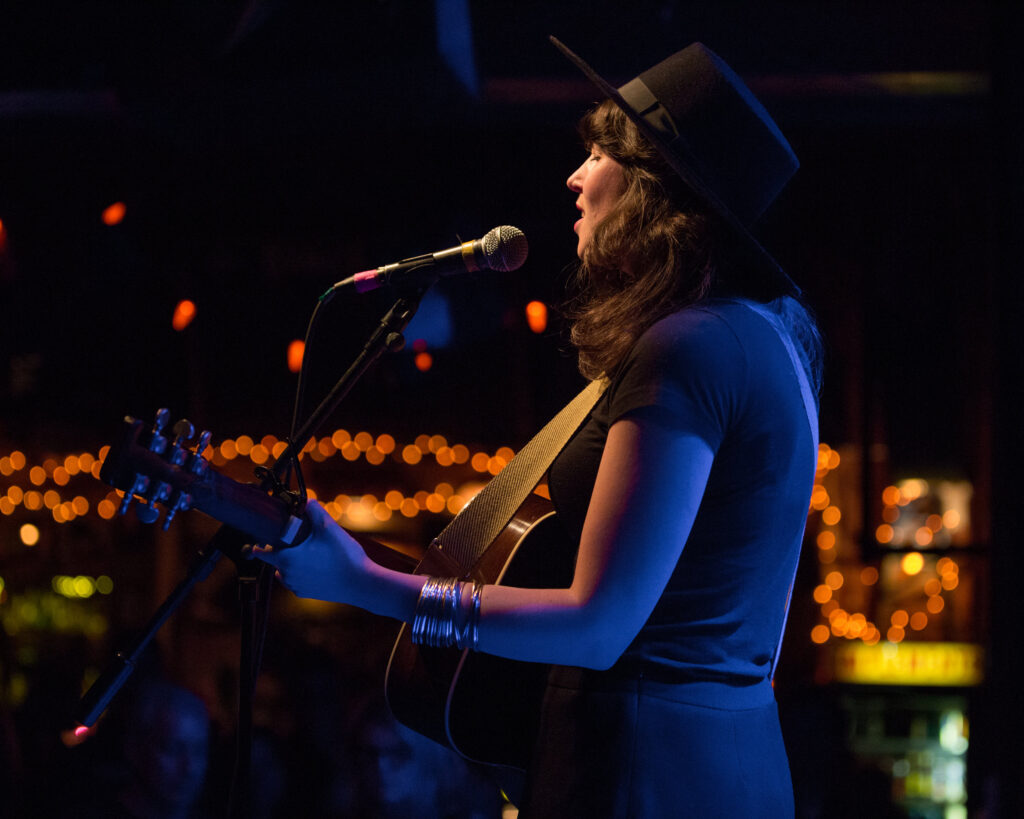 Musician Lydia Ramsey playing a guitar and singing on stage.