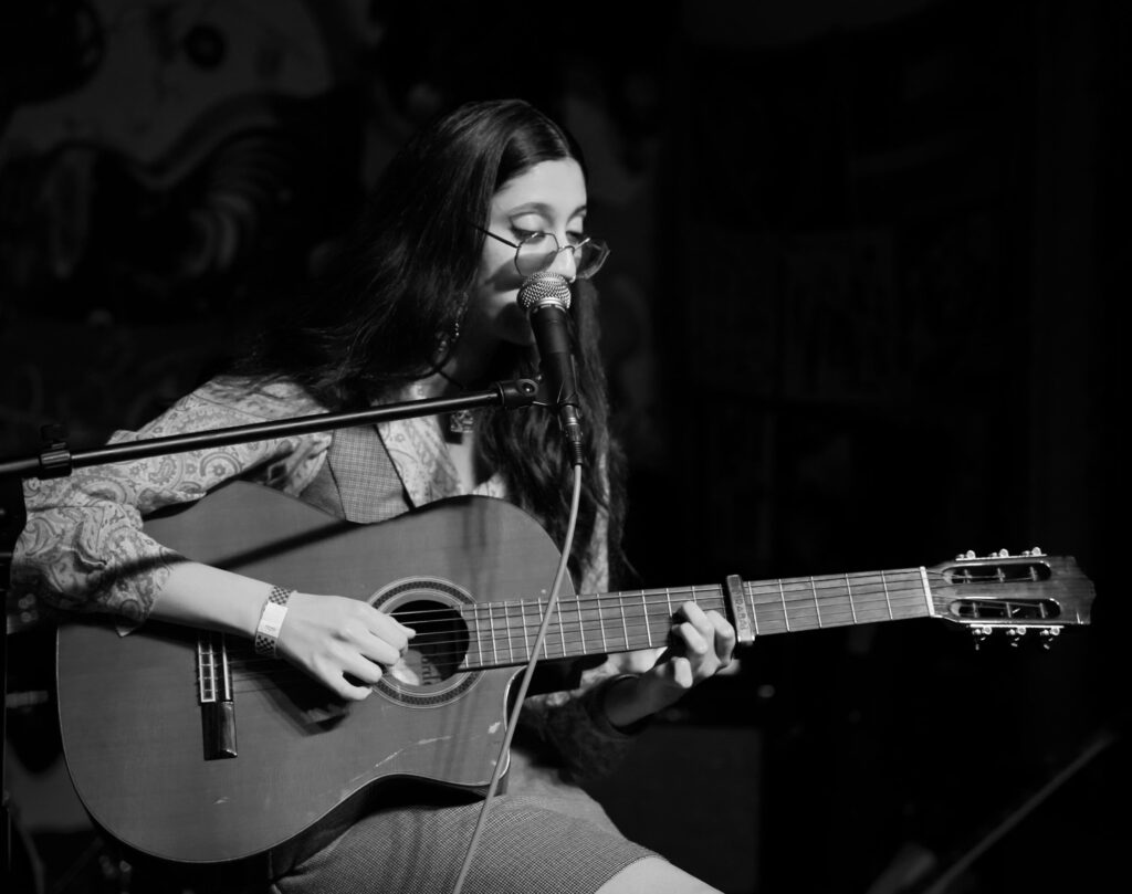 A photo of artist Mirabai holding a guitar in front of a microphone.