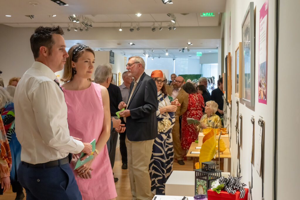 Couple in foreground at an exhibit, looking at wall-mounted displays in a bright gallery space.