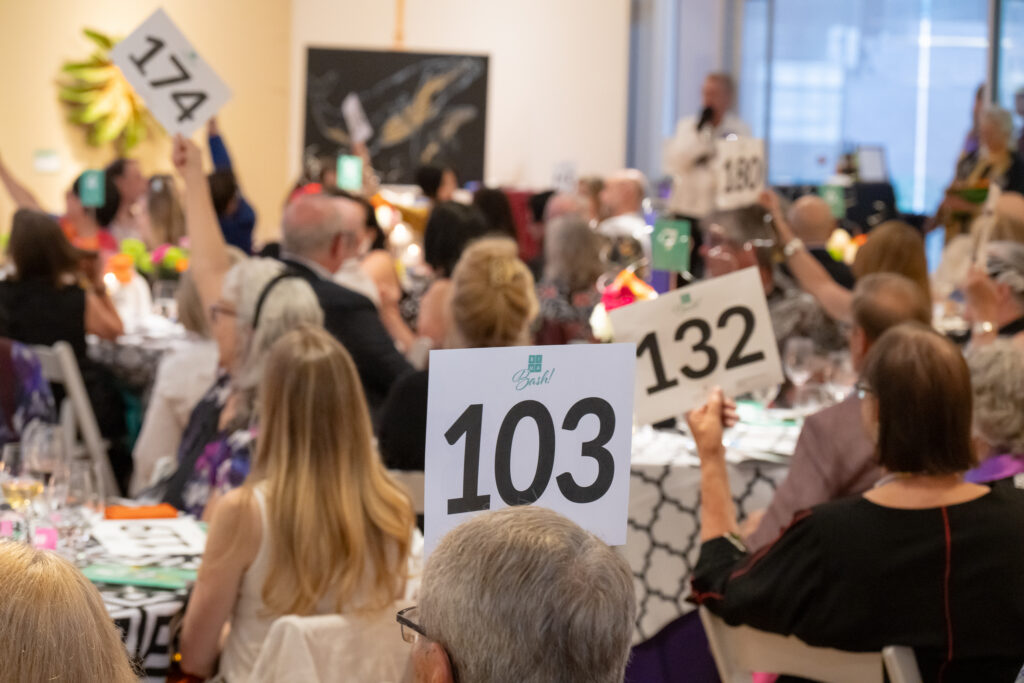 Crowd of guests seated at tables during a banquet with large number signs 103 and 132 visible in the foreground.