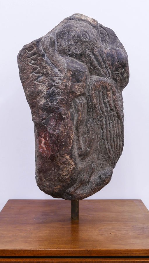 Dark, abstract stone sculpture mounted vertically on a wooden base, featuring carved textures and symbolic forms.