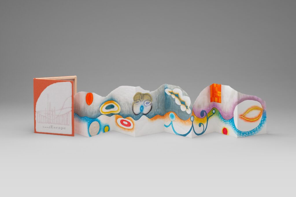 An accordion-fold artist book with a red and white cover. The unfolded pages show colorful abstract shapes and patterns in bright orange, blue, yellow, and purple.