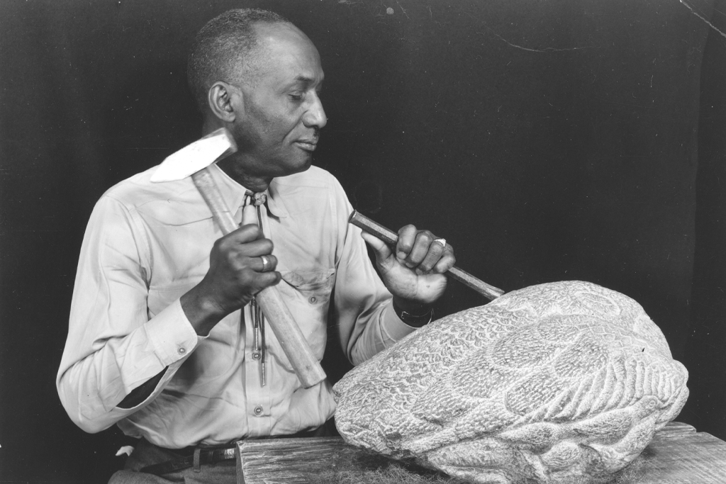 Black and white photo of man carving a stone with handtools