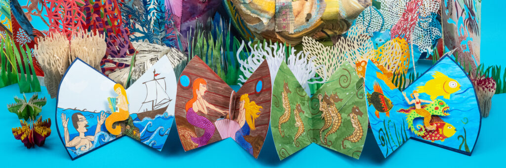 Accordion-style artist book with colorful, cut-paper illustrations depicting marine life and underwater scenes, displayed against a bright blue background.