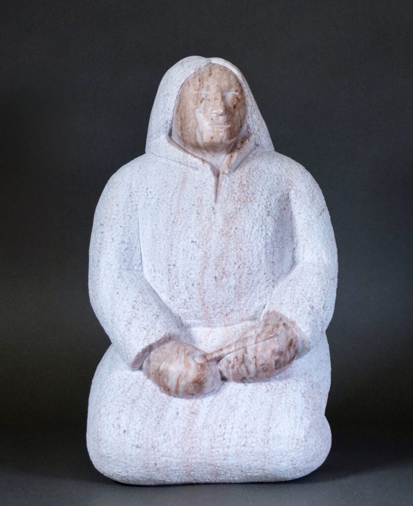 Stone statue of a robed figure with hands clasped in front, wearing a hood against a dark background.