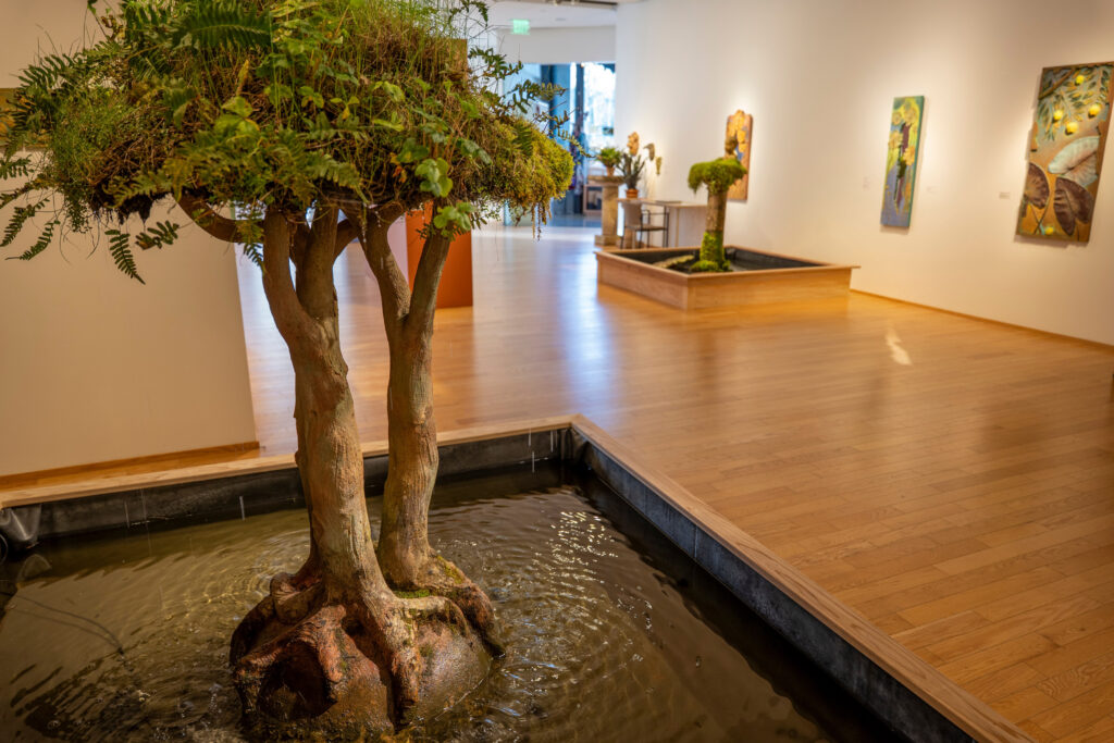 A concrete sculpted tree sits in a running fountain in the foreground.
