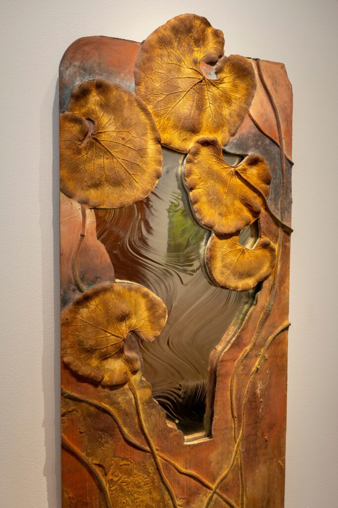 A vertical mirror hangs on a white wall and is enclosed with painted (brown) cement in the shape of water lillies.