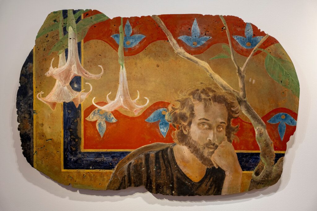 Painted on a piece of concrete is a man with his head in his hand, and behind him flowers bloom off a tree.