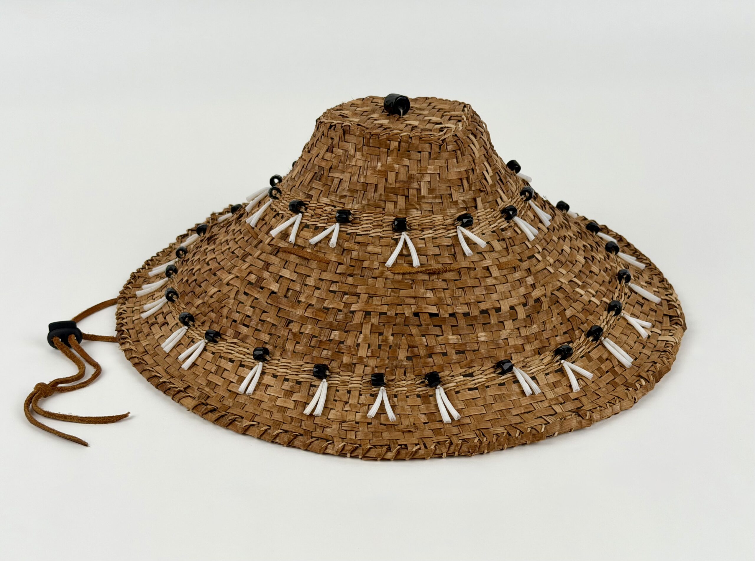 Wide-brimmed woven straw hat with white tassels and black beads against a light background