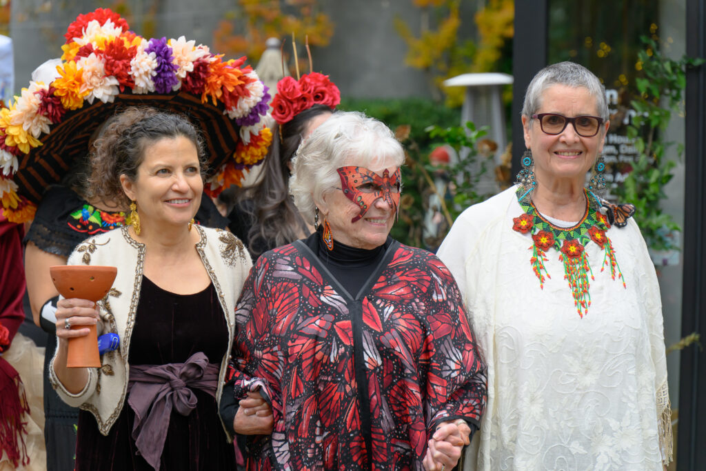 Three women walk in a procession for Dia de los Muertos.