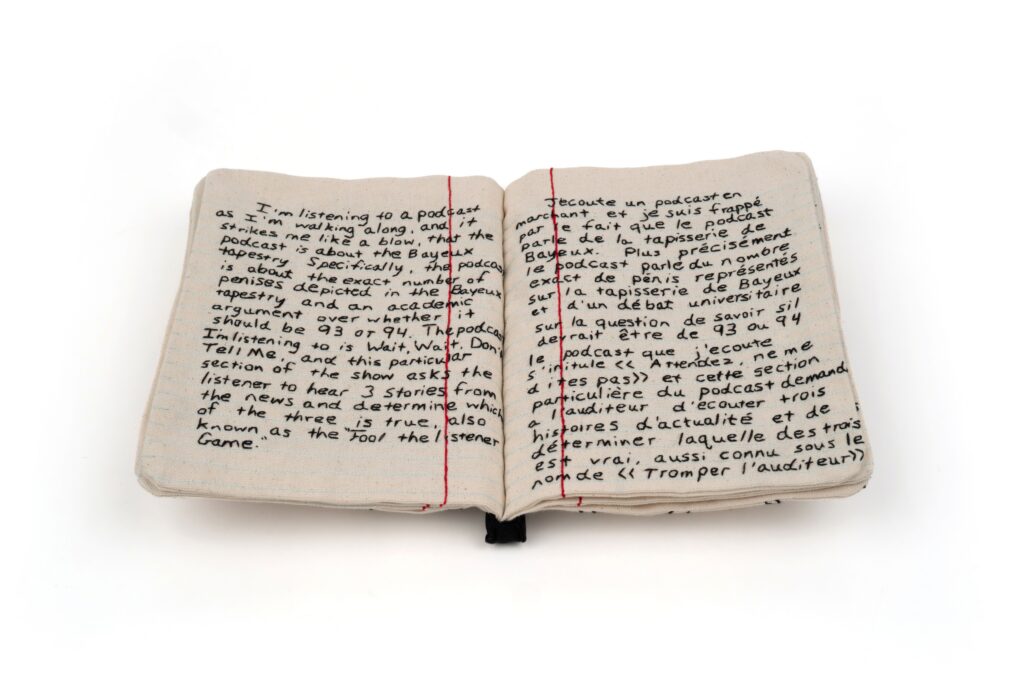An open book made of canvas that looks like a notebook the pages are filled with embroidered writing