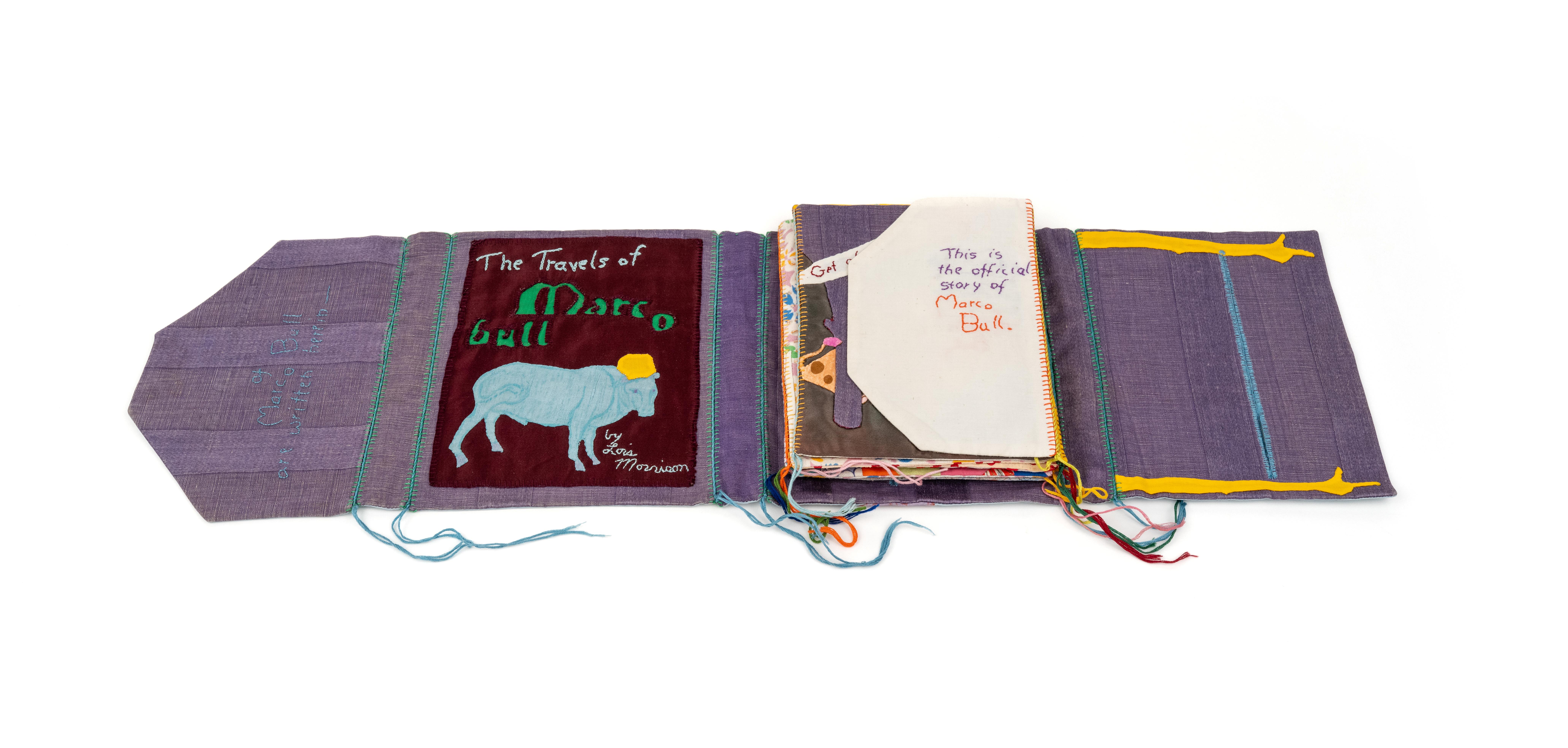 A purple book made of fabric with the cover open On the inside cover it says the travels of marco bull with an image of a blue bull
