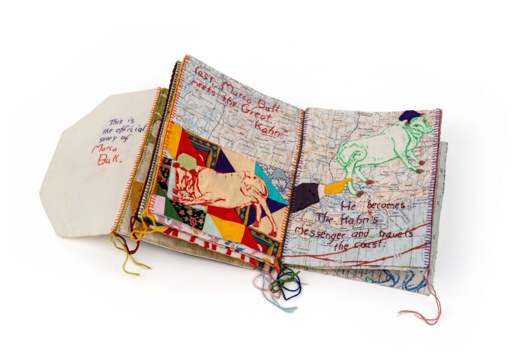 An open book made of fabric The pages have maps on them embroidered bulls and text
