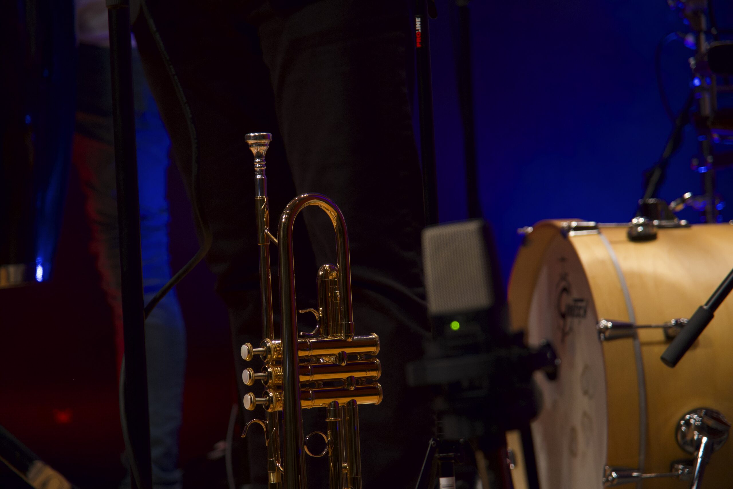 Close up of a gold trumpet on a dimly lit concert stage with a bass drum visible in the background