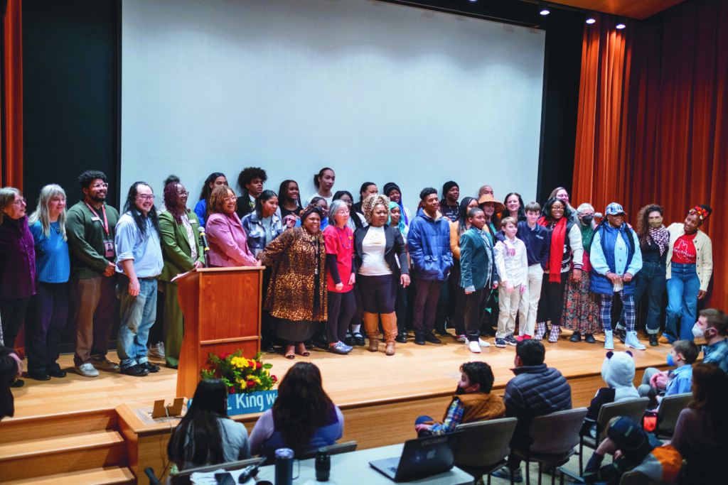 A large group of people stand on stage in the Auditorium,